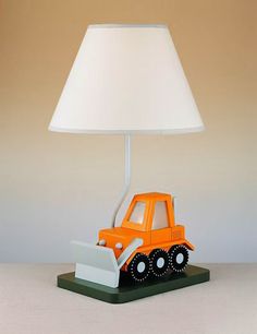 an orange toy truck under a white lamp on a green base with a white shade