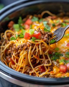 a fork in a slow cooker filled with taco pasta and meat, garnished with cilantro