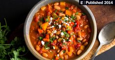 a bowl of beans and carrots on a wooden board with a spoon next to it