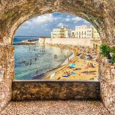 people are on the beach under an arched stone archway that overlooks the ocean and buildings