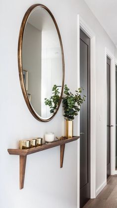 a mirror and some candles on a shelf in a hallway next to a wall mounted plant