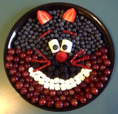 a plate that has fruit in the shape of a cat on top of berries and grapes