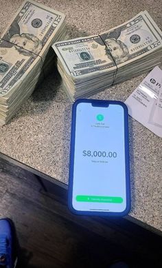 a cell phone sitting on top of a counter next to stacks of $ 8, 000 bills