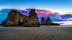 the beach is covered in sand as the sun sets behind some large rocks and boulders