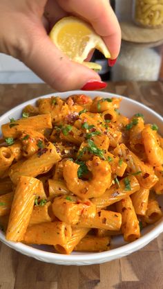 a person is holding a lemon over a bowl of pasta with sauce and parsley