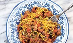 a blue and white plate topped with pasta covered in sauce, parmesan cheese and meat