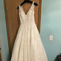 a white wedding dress hanging on a wooden hanger in front of a blue wall