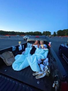 two women laying in the back of a pick - up truck with blankets on it