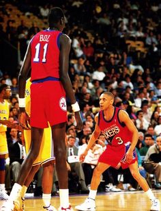 two basketball players in red and blue uniforms are standing on the court while an audience watches