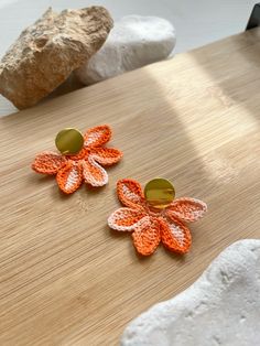 two orange and white crocheted flower earrings on a wooden surface next to rocks