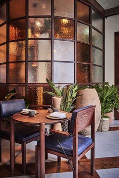 a table with two chairs and a vase on it in front of a window filled with plants