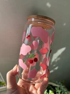 a hand holding up a glass with hearts and cherries on the inside, in front of a plant