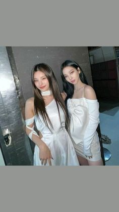 two young women standing next to each other in front of a metal wall and door