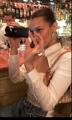 a woman holding up a camera in front of her face while sitting at a bar