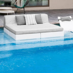 a couch sitting on top of a blue pool next to a white chair and table