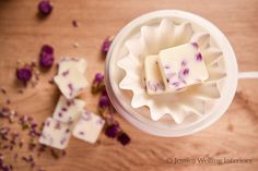 two pieces of soap sitting on top of a wooden table next to purple flower petals