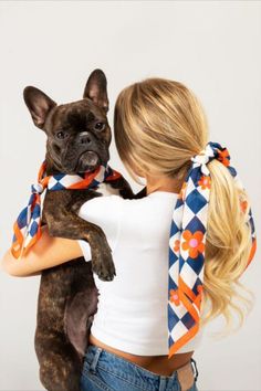 a woman holding a dog in her arms with an orange and blue scarf around it's neck