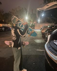 a man holding a skateboard in front of his car with the hood open and headlight on