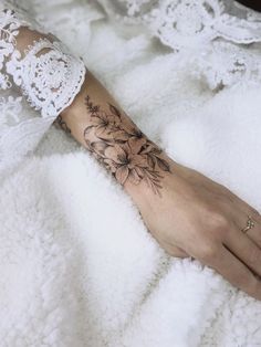 a woman's hand with a flower tattoo on her left arm and the wrist is covered in lace