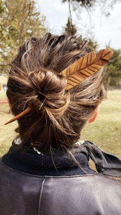 the back of a woman's head with a feather in her hair and an arrow sticking out of it