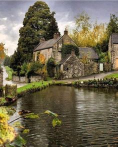 an old stone house sitting next to a body of water in the middle of a lush green forest