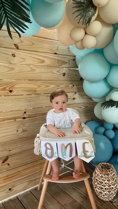 a baby sitting in a high chair next to balloons