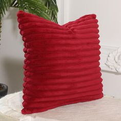 a red pillow sitting on top of a white bed next to a plant in a room