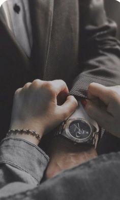 a man in a suit adjusting his watch on another mans wrist while wearing a bracelet