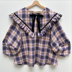 a purple and yellow plaid shirt with ruffles on the collar, sitting on a hanger