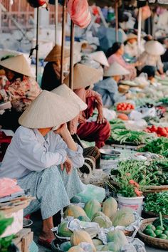 two women sitting on the ground with hats over their heads and vegetables in baskets behind them