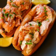 two lobster sandwiches with lemon wedges on a black plate, ready to be eaten