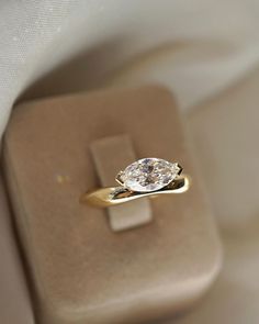 a diamond ring sitting on top of a white cloth covered box with a gold band