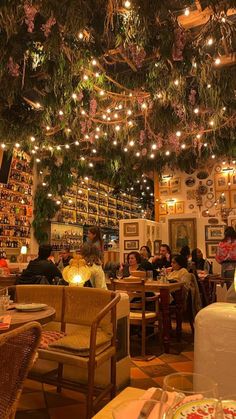 people sitting at tables in a restaurant with lots of lights hanging from the ceiling above them