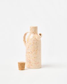 a small white vase with sprinkles next to a cork stopper on a white background