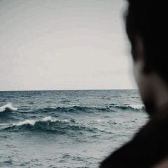 a person standing in front of the ocean looking out at the waves on the water