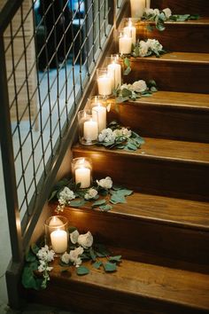 candles are lined up on the stairs with flowers and greenery