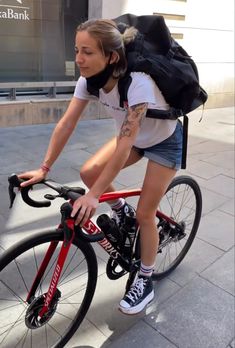 a woman on a bike with a backpack strapped to her back riding down the street