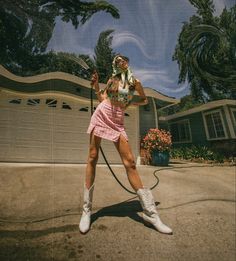 a woman in a pink dress is holding a hose and posing for the camera with her hands behind her head