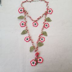 a necklace with flowers and leaves hanging from it's sides on a white surface