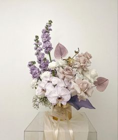 a vase filled with purple and white flowers sitting on top of a glass table next to a wall