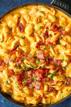 a skillet filled with macaroni and cheese covered in bacon on top of a blue surface