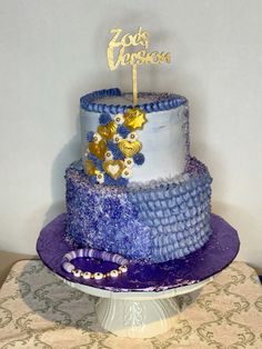 a three tiered cake with blue and white frosting, gold decorations and a name on top