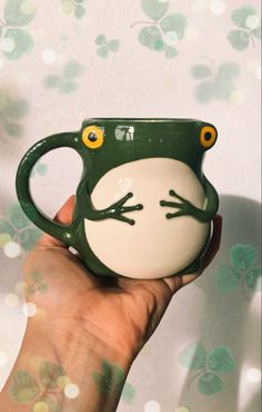 a hand holding a green and white frog mug