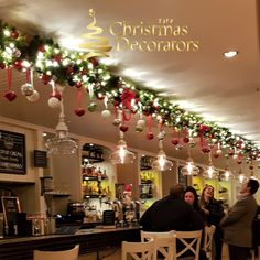 people sitting at tables in a restaurant with christmas decorations hanging from the ceiling