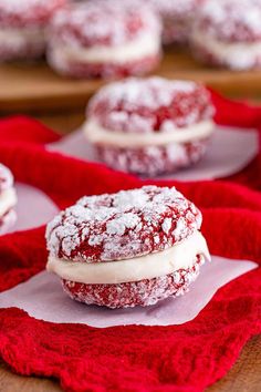 red velvet cookies covered in powdered sugar on top of a red cloth with white frosting