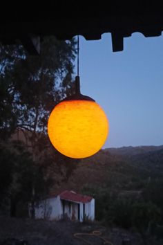 a yellow light hanging from the side of a building in front of trees and mountains