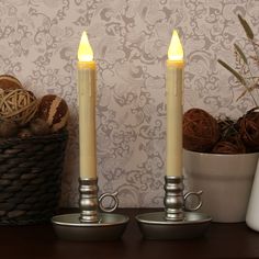 two lit candles sitting on top of a wooden table next to a basket with balls of yarn