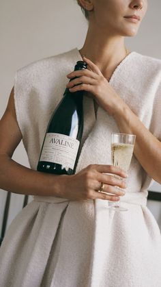 a woman is holding a wine bottle and a glass in her hand while wearing a white dress