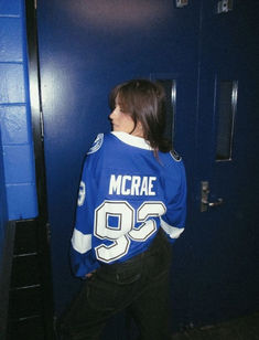 a girl in a hockey jersey is standing by a locker door and looking at something