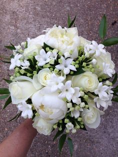 a bridal bouquet with white flowers is held by someone's hand on the pavement